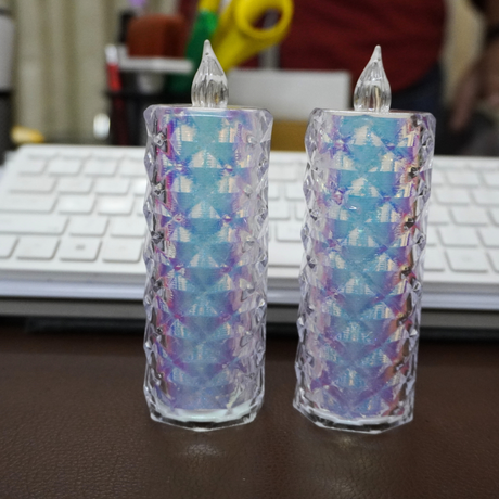 Two decorative candles with a colorful pattern on a desk in front of a laptop.