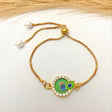 Gold bracelet with a peacock feather charm on a white background